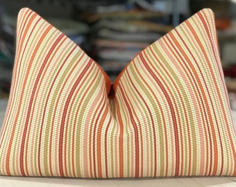 May include: A striped pillow with a cream background and red, orange, and green stripes. The pillow is made of a woven fabric and has a slightly textured surface.