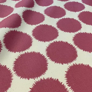May include: Close-up of a fabric with a repeating pattern of large, maroon-colored circles with spiky edges against a cream-colored background. The fabric has a soft, slightly wrinkled texture.
