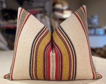May include: A white pillow with red, yellow, black, and gray striped pattern. The pillow is made of a woven fabric.