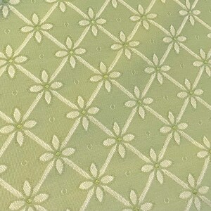 May include: A close-up of a green fabric with a white floral pattern. The fabric has a subtle texture and a repeating pattern of small white flowers.