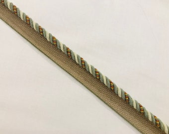 May include: A beige and green braided trim with a white and red stripe. The trim is woven with a textured fabric.