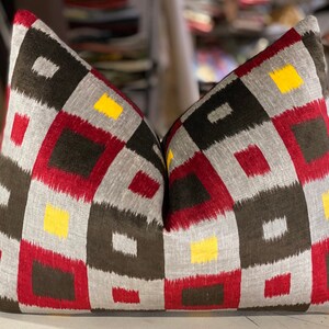 May include: Two decorative throw pillows with a geometric pattern in shades of red, black, gray, and yellow.