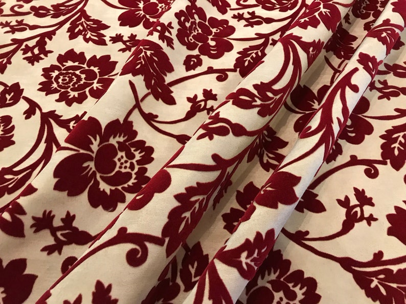 K&ouml;nnte beinhalten: Roter Samtstoff mit wei&szlig;em Hintergrund und einem floralen Muster. Der Stoff hat eine erhabene Textur und ein luxuri&ouml;ses Gef&uuml;hl.
