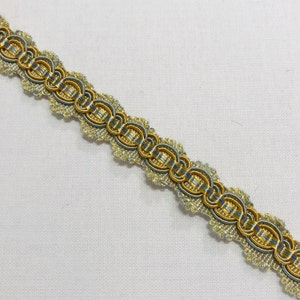 May include: A close-up of a gold and silver trim with a scalloped edge. The trim is made of woven fabric and has a decorative pattern.