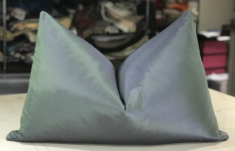 May include: A soft, iridescent pillow with a light blue and green color gradient. The pillow is made of a smooth, silky fabric and has a simple, rectangular shape.