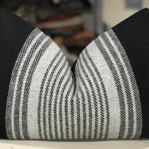May include: Black and white striped throw pillow with black fabric trim. The pillow is made of a soft, textured fabric.