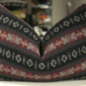 May include: A decorative pillow with a black, gray, red, and white geometric pattern. The pillow is made of a soft, textured fabric.