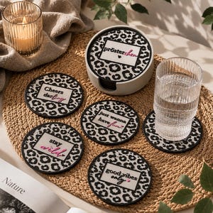 Könnte beinhalten: Ein Set aus fünf runden Untersetzern mit schwarz-weißem Leopardenmuster. Jeder Untersetzer hat ein weißes Quadrat in der Mitte mit schwarzem Text, der Cheers darling, just wanna have fun, stay wild, good vibes only und prösterchen lautet.