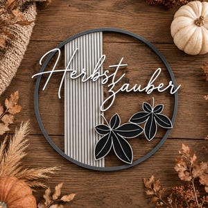 Könnte beinhalten: Ein rundes Wandschild mit dunklem Rahmen, einem vertikalen, hellgrauen Lamellenpaneel und zwei schwarzen Blattausschnitten. Der weiße Schriftzug "Herbstzauber" ist mittig angebracht. Das Design kombiniert geometrische Linien mit organischen Formen.