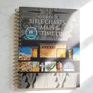May include: A spiral-bound book titled "Rose Book of Bible Charts, Maps & Time Lines" with a 10th Anniversary emblem. The cover features architectural illustrations and a collage of images. The book has a gold spiral binding.