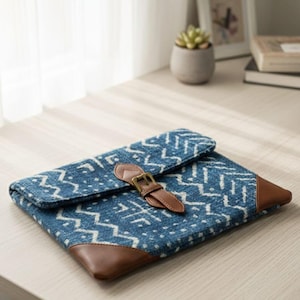 Pode incluir: Uma clutch azul e branca estampada com detalhes em couro castanho. A clutch apresenta um fecho de aba com uma correia de couro castanho e uma fivela dourada. Os cantos são reforçados com couro castanho.