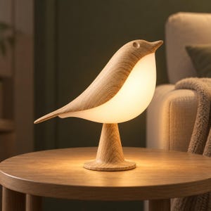 Könnte beinhalten: Eine vogelförmige Tischleuchte mit einer hellen Holzmaserung an Kopf, Rücken und Fuß sowie einem glatten, weiß leuchtenden, durchscheinenden Körper, der ein sanftes, warmes Licht abgibt und auf einem runden Sockel steht.
