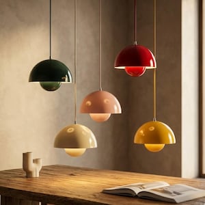 Puede incluir: Cinco lámparas colgantes de varios colores cuelgan del techo. Las lámparas tienen una parte superior redondeada en forma de cúpula y una parte inferior esférica. Los colores incluyen verde oscuro, rosa, rojo, amarillo y crema. Las lámparas están suspendidas sobre una mesa de madera.
