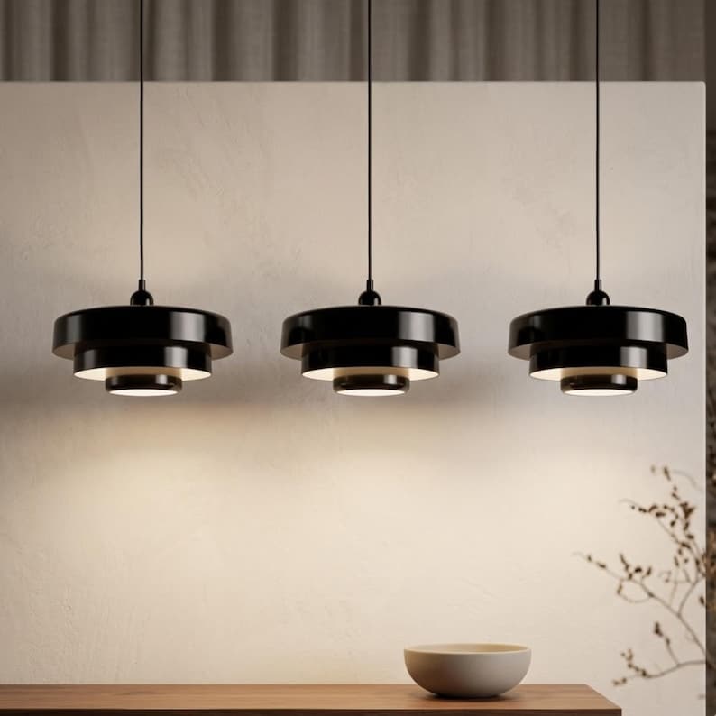 Pode incluir: Tr&ecirc;s candeeiros suspensos pretos com um design circular de v&aacute;rios n&iacute;veis, pendurados por cabos pretos finos. Cada candeeiro apresenta um acabamento brilhante no exterior e um interior branco, projetando luz para baixo.
