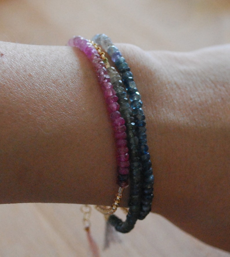 May include: Three layered bracelets with pink, blue, and gray gemstone beads. The bracelets are on a person's wrist.