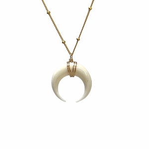 Peut inclure: Un collier en chaîne dorée avec un pendentif en forme de croissant de lune blanc. Le pendentif est enveloppé de fil doré.