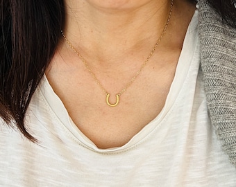 Könnte beinhalten: Eine goldene Hufeisen-Anhänger-Kette an einer zarten Kette. Das Hufeisen ist ein Symbol für Glück und Vermögen.