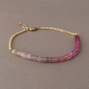May include: A delicate gold chain bracelet with a gradient of pink and white gemstones. The bracelet is made with small, round beads that are strung together in a continuous line.