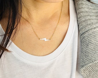 May include: A gold chain necklace with a small lightning bolt pendant.