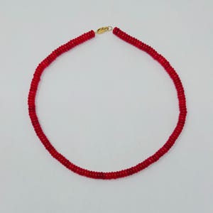 May include: A red beaded necklace with a gold-colored clasp. The necklace is composed of small, round, red beads strung together to form a circular shape. The clasp is a simple hook and eye closure.