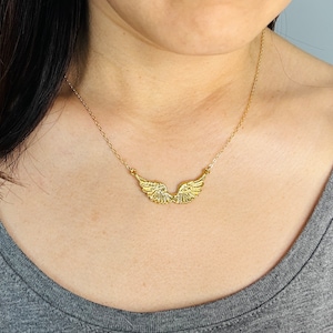 Puede incluir: Un collar de oro con un delicado colgante de alas. Las alas son detalladas y tienen un acabado texturizado.