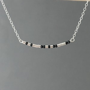 May include: A silver chain necklace with a delicate row of black beads and silver spacers.
