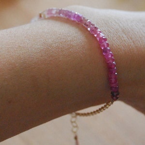 May include: A pink and white gemstone bracelet with a gold chain clasp.