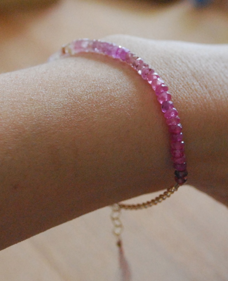 May include: A pink and white gemstone bracelet with a gold chain clasp.