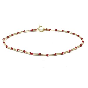 May include: A gold bracelet with red string accents. The bracelet is made of small, thin gold bars connected by red string.