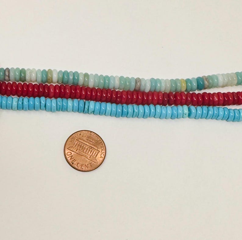May include: Close-up of four strands of colorful beads. The top strand features a mix of light blue, green, and white beads. Below it is a strand of red beads, followed by a strand of turquoise beads. A penny is in the foreground.