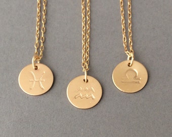 May include: Three gold-colored necklaces with circular pendants. Each pendant features a different zodiac symbol: Pisces, Aquarius, and Libra. The chains are delicate, and the pendants are small and round, with the symbols etched into the metal.