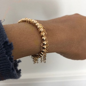 May include: A gold bracelet with a chain of small round beads and a fringe of dangling chains.