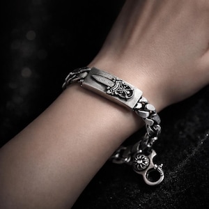 May include: A silver-colored bracelet with a thick chain design. The bracelet features a rectangular centerpiece with the word "CHROME" and a decorative emblem. The clasp is a round, ornate design.