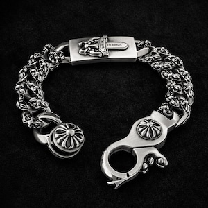May include: A silver bracelet with a floral chain design. The clasp features a decorative flower and the text "HEARMS". The bracelet is made of a shiny metal and is displayed against a dark background.