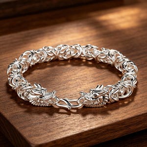 Könnte beinhalten: Ein silbernes Armband mit einem Drachendesign. Das Armband hat aufwendige Glieder und Drachenkopfverschlüsse. Der Schmuck wird auf einer Holzoberfläche präsentiert.