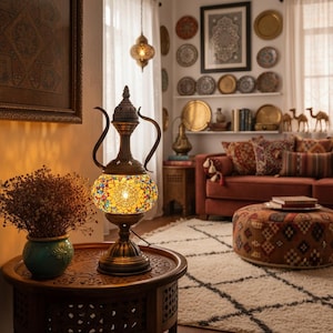 Puede incluir: Lámpara de mesa decorativa con globo de mosaico de vidrio y marco de metal color bronce. La lámpara está sobre una mesa de madera oscura, con un jarrón de flores secas y una alfombra estampada en el fondo. La habitación tiene un estilo bohemio.