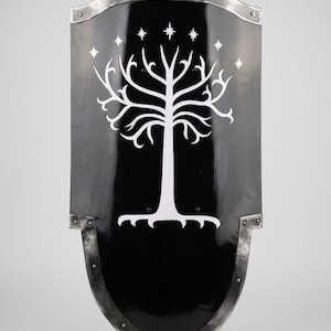 May include: A black shield with a white tree and star design. The shield has a metallic border and rivets. The design is reminiscent of a fantasy theme, possibly for cosplay or display.