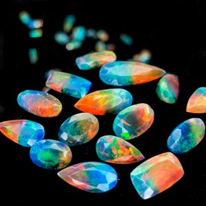 May include: A collection of faceted loose opals featuring a play of color with vibrant flashes of orange, blue, and green. These gemstones are cut into various shapes including ovals, pears, and rectangles, displaying a translucent quality.