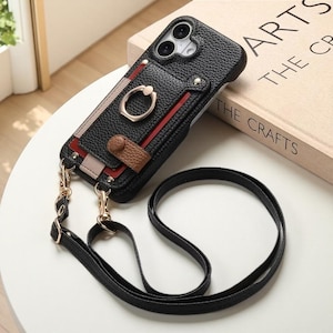 Puede incluir: Funda de teléfono de cuero negro con ranura para tarjetas, soporte de anillo y correa negra desmontable. La funda tiene herrajes dorados y un acento de cuero marrón. La funda está sobre una superficie blanca.