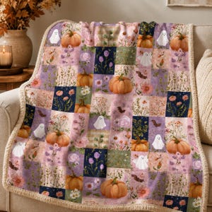May include: A soft throw blanket featuring a patchwork design of autumn-themed squares. The pattern includes illustrations of orange pumpkins, white ghosts, small brown bats, and various floral arrangements in shades of pink, purple, and green.