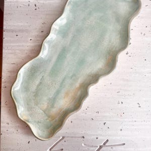 May include: A pale blue ceramic serving platter with a wavy edge. The platter has a watercolour effect with shades of blue and green. The word "Entree" is carved into the surface below the platter.