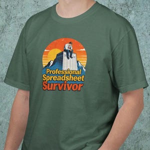 May include: A forest green t-shirt featuring a graphic of a person sitting on top of a skyscraper against a sunset. The text reads Professional Spreadsheet Survivor in yellow and orange letters. The design has a retro aesthetic with a circular background.