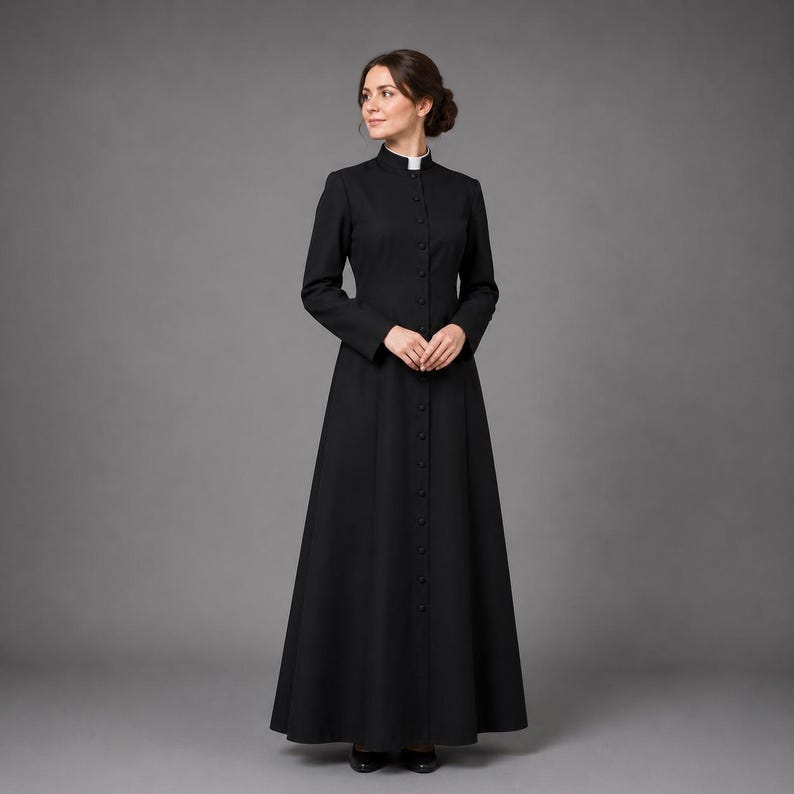 May include: A long, black dress with a high, rounded collar and long sleeves. The dress is buttoned down the front and flares out from the waist. A white collar is visible at the neck. The dress is worn with black shoes.