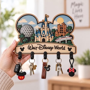 Puede incluir: Un llavero de pared de madera con forma de orejas de Mickey Mouse, con un diseño en capas del parque Walt Disney World que incluye un castillo, un monorraíl y una esfera. El texto Walt Disney World está impreso con cinco ganchos negros.