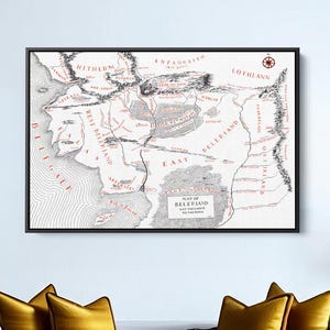 Puede incluir: Un mapa enmarcado de una tierra ficticia, con detalles geográficos y texto. El mapa es en blanco y negro con detalles en rojo, colgado sobre un sofá blanco con cojines dorados y una manta negra. Una mesa de centro de madera y una planta en maceta completan la escena.