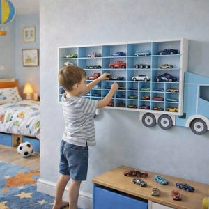 Puede incluir: Un estante de pared con forma de camión azul claro con un remolque rectangular blanco que cuenta con múltiples compartimentos. El estante está lleno de varios coches de juguete pequeños y la cabina del camión incluye dos ruedas grises.
