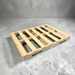 May include: A small, rectangular wooden pallet constructed from light-colored, smooth-finished slats. The structure features a series of parallel horizontal boards spaced evenly apart, supported by perpendicular base beams, creating a grid-like design.