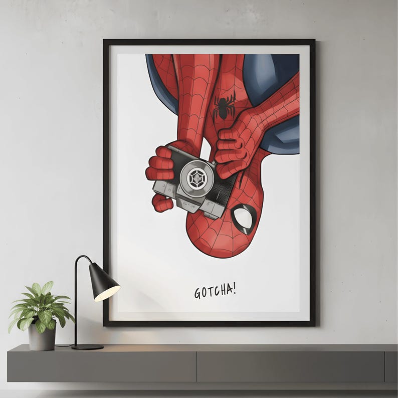 May include: A framed print featuring Spider-Man holding a vintage camera. The superhero is depicted in his classic red and blue suit, with the text "GOTCHA!" below the image. The artwork is set against a white background.