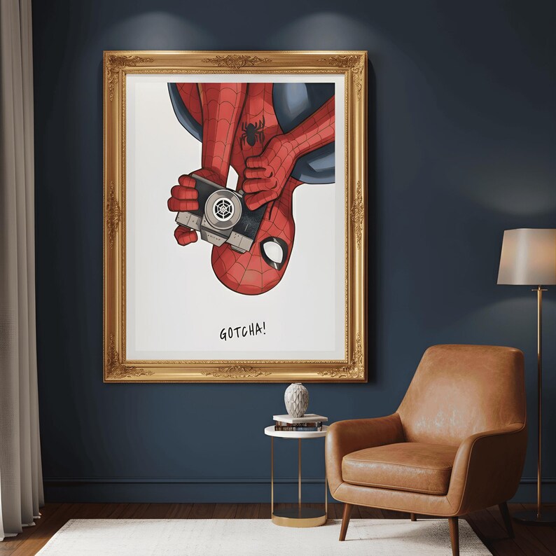 May include: A framed art print featuring Spider-Man holding a vintage camera. The illustration shows Spider-Man upside down, with his red and black suit and the text "GOTCHA!". The frame is gold.