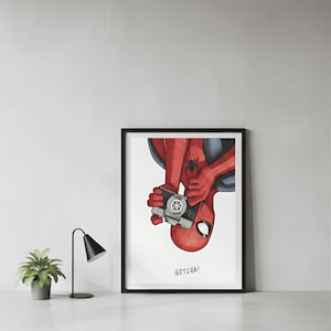 May include: Framed art print featuring a comic-style illustration of Spider-Man holding a camera. The superhero is depicted in his classic red and blue suit, with the word "GOTCHA!" below the image. The artwork is set against a white background.